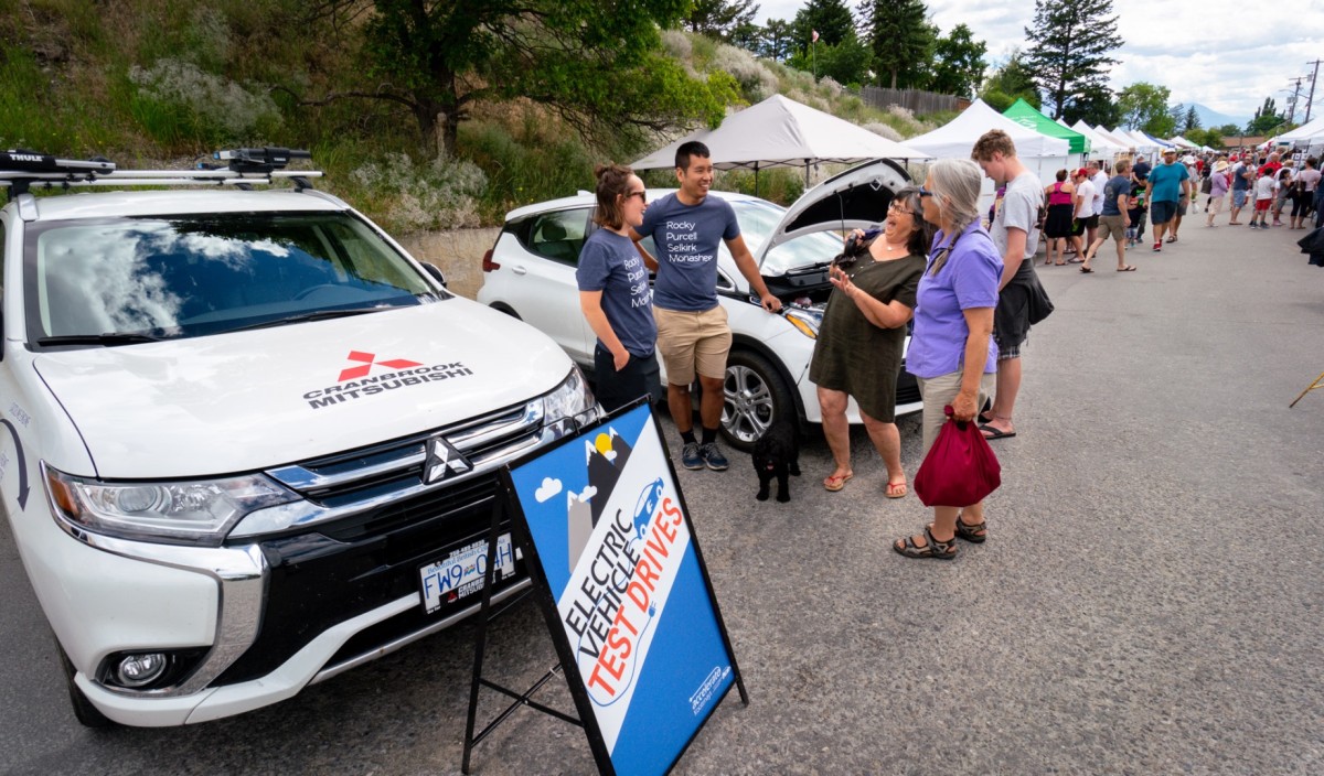 Electric cars on display with a sign in front and four people talking