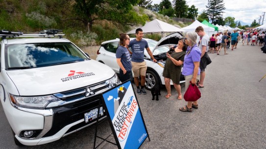 Electric cars on display with a sign in front and four people talking