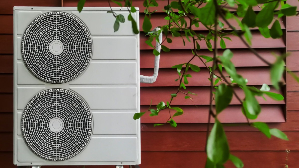 external heat pump fan on side of house with green leaves in the foreground