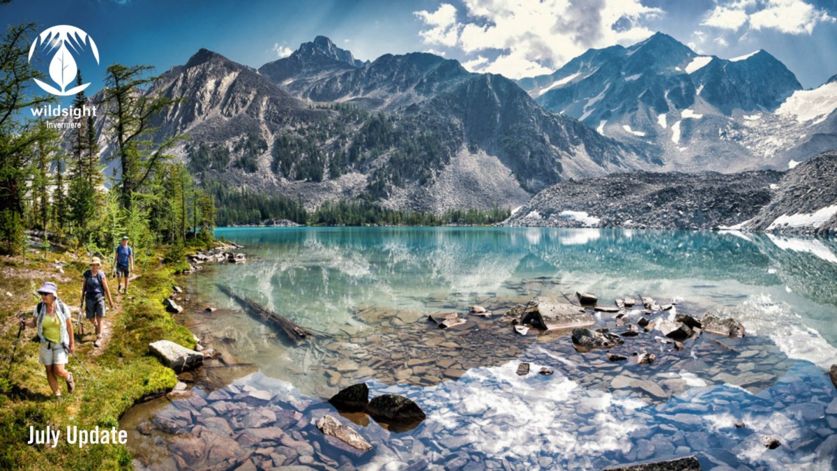 Photo of three people hiking beside mountain lake