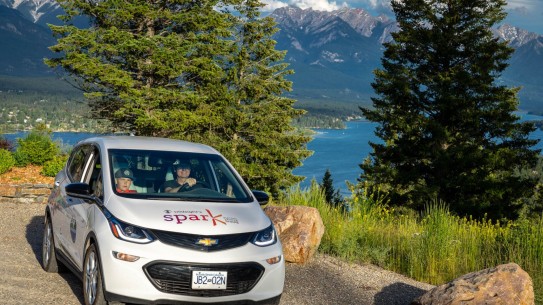 Electric vehicle parked with trees, lake and mountains behind it