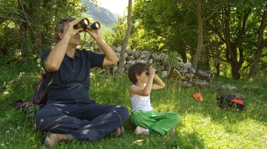 An adult and child sitting on grass looking through binoculars