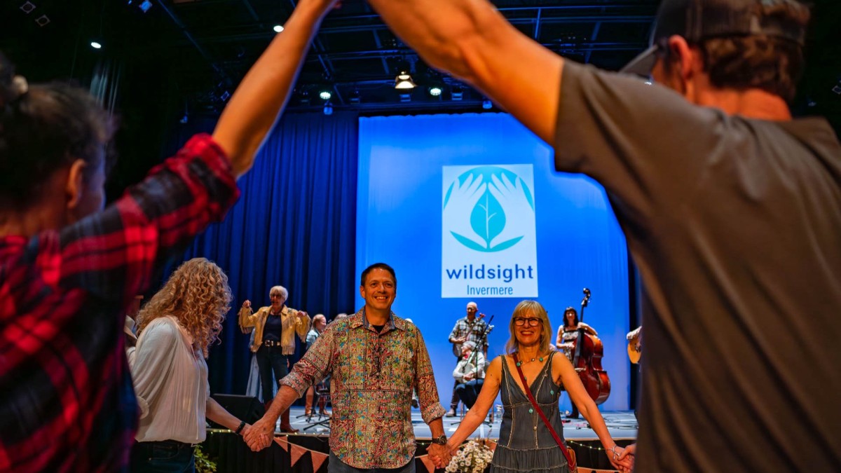 Smiling people holding hands in a circle, with musicians behind them on a stage