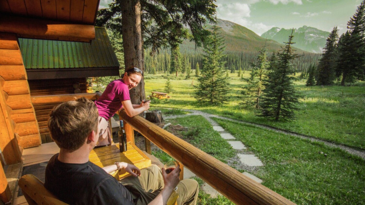 Photo of two people looking out from log cabin balcony to a forested valley