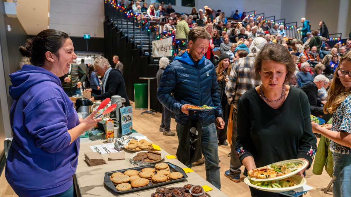 a laughing volunteer serving baked goods to people with plates, in a crowded hall