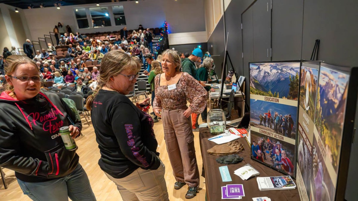 Two people looking at posters on a table, in a hall full of people